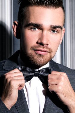 şeritli bir arka plan üzerinde koyu takım elbise ve kravat takan yakışıklı adam sakallı bir poz