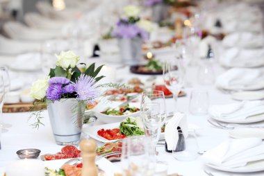 Bir kutlamada, içinde çiçekler ve bir sürü farklı yiyecek olan büyük bir yemek masası.