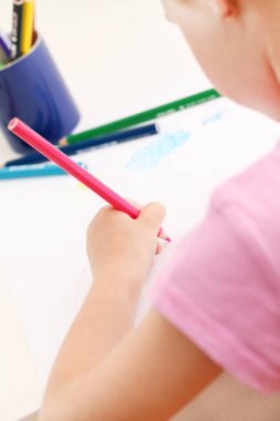 Kağıda renkli kalemlerle resim çizen sevimli küçük kız.