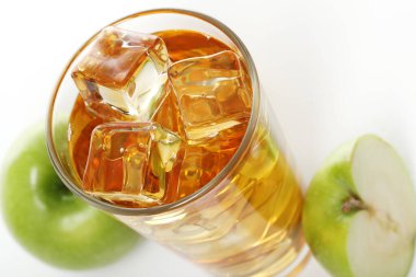 Bir bardak buzlu elma suyu ve beyaz arka planda duran elmalar.