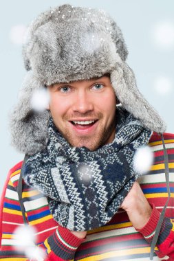 kar mavi arka plan üzerinde düşerken bir kürk şapka yakışıklı bir adam, bir eşarp ve çizgili kazak poz