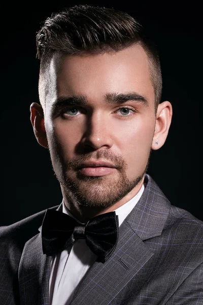 Siyah arka planda poz veren takım elbiseli yakışıklı bir adamın portresi.