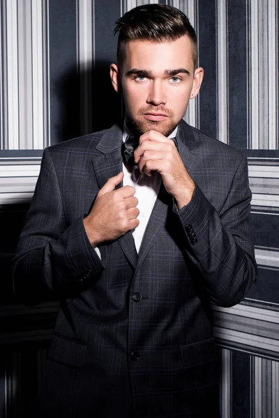 şeritli bir arka plan üzerinde koyu takım elbise ve kravat takan yakışıklı adam sakallı bir poz