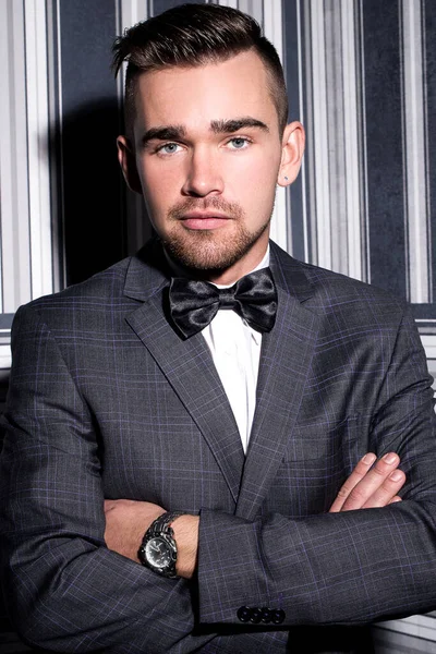 şeritli bir arka plan üzerinde koyu takım elbise ve kravat takan yakışıklı adam sakallı bir poz