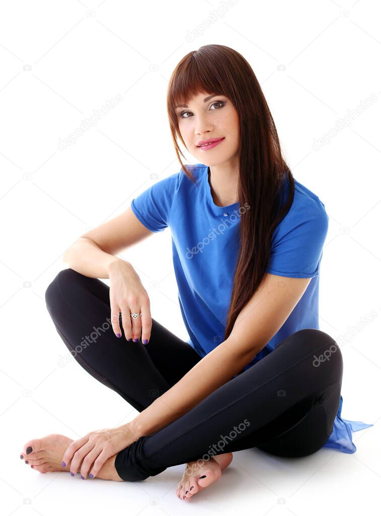 Beautiful woman in leggings and a blue shirt is sitting on the floor and posing
