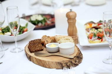 Ekşi kremalı iki farklı ekmek ve tahta bir tabakta duran tahta bir kaşık.