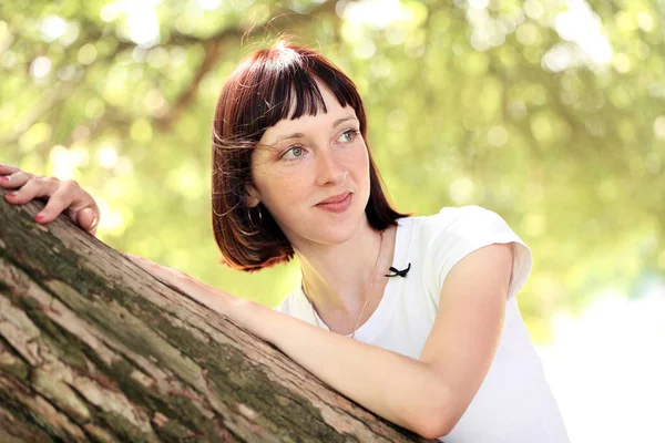 Kadın parkta bir ağacın yanında poz veriyor.