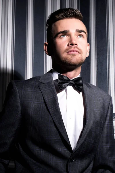 şeritli bir arka plan üzerinde koyu takım elbise ve kravat takan yakışıklı adam sakallı bir poz