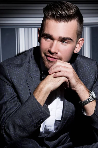 şeritli bir arka plan üzerinde koyu takım elbise ve kravat takan yakışıklı adam sakallı bir poz