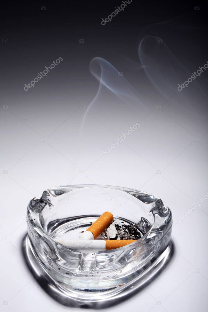 Cigarette in the ashtray over gray gradient