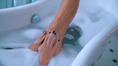 Lüks banyoda köpükle rahatlayan seksi genç kadın.