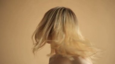 Sarı saçlı, bej arka planda kameraya poz veren doğal bir genç kadın portresi. 