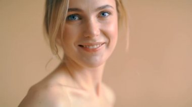 Sarı saçlı, bej arka planda kameraya poz veren doğal bir genç kadın portresi. 