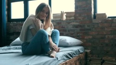 Evdeki yatakta kameraya poz veren bir kadın. 