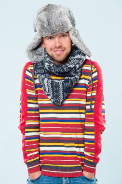 yakışıklı erkek çizgili kazağı, eşarp ve mavi bir arka plan üzerinde poz kürklü şapka