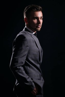 Siyah arka planda poz veren takım elbiseli yakışıklı bir adamın portresi.