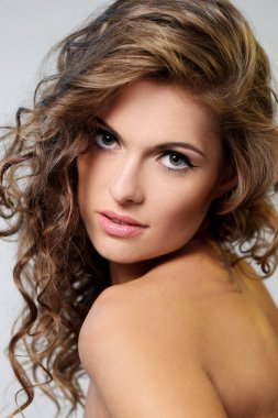 kıvırcık saçlı ve hafif bir arka plan üzerinde poz çıplak omuzlarına güzel esmer bir kadın portresi