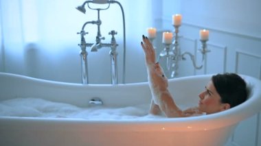 Lüks banyoda köpükle rahatlayan seksi genç kadın.