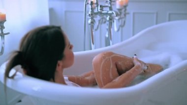 Lüks banyoda köpükle rahatlayan seksi genç kadın.