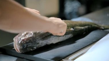 Kadın aşçı mutfakta bıçakla balığı kesiyor. 