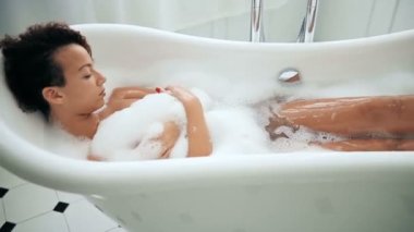 Güzel Afrikalı Amerikalı kadın köpükle banyoda dinleniyor. 
