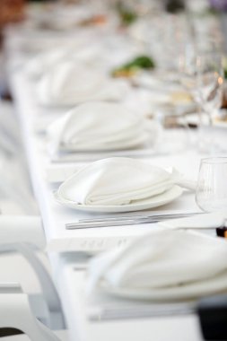 Lokantada katlanmış peçeteli bir sürü sandalye ve tabakla kutlama masası.