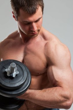 Gri arka planda izole edilmiş dambıllarla çalışan yakışıklı bir adam.