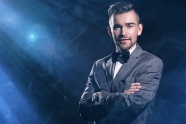 Siyah arka planda poz veren takım elbiseli yakışıklı bir adamın portresi ve üzerine mavi ışınlar düşüyor.