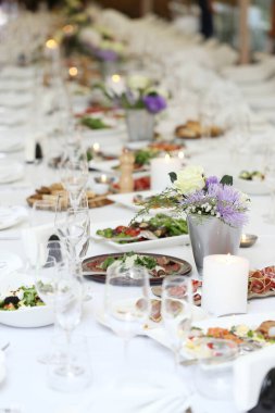 Bir kutlamada, içinde çiçekler ve bir sürü farklı yiyecek olan büyük bir yemek masası.