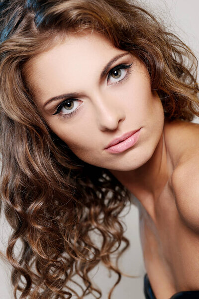 Portrait of a beautiful brunette woman with curly hair and naked shoulders posing over a light background