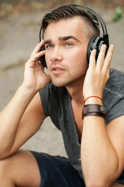 一个英俊的男人坐在街边听音乐的耳机的肖像 — 图库照片