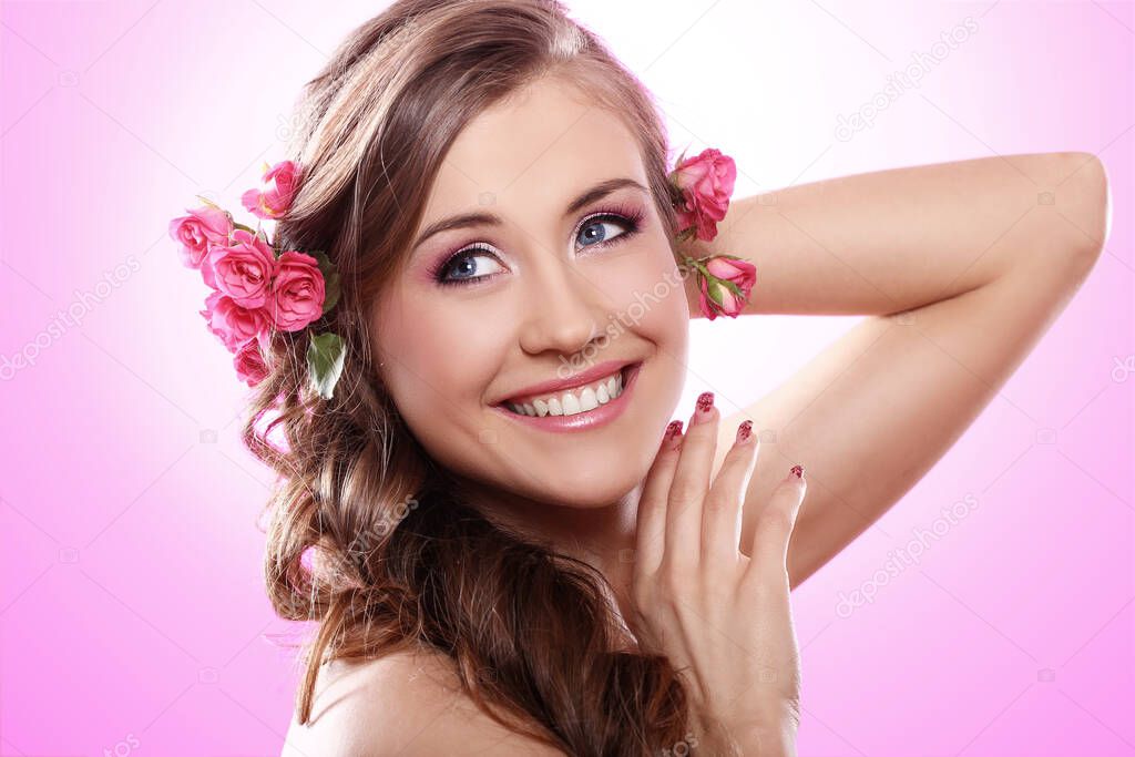 Beautiful woman with roses in hair over pink background