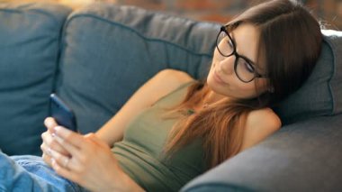 Evde akıllı telefon kullanan genç bir kadın.