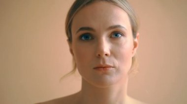 Sarı saçlı, bej arka planda kameraya poz veren doğal bir genç kadın portresi. 