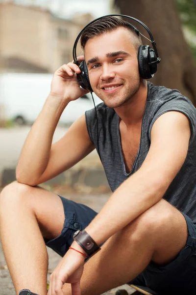 一个英俊的男人坐在街边听音乐的耳机的肖像 — 图库照片
