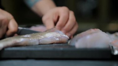 Kadın aşçı mutfakta bıçakla balığı kesiyor. 