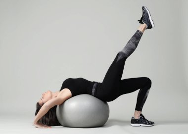 Beyaz arka planda büyük topla egzersiz yapan bir kadın.