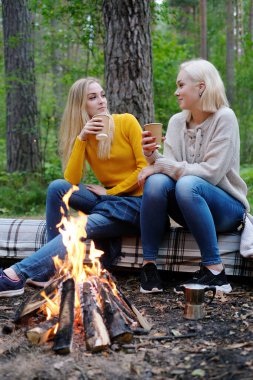 Seyahat ve keşfetmek. Ormandaki şenlik ateşi yakınındaki iki genç güzel kadın