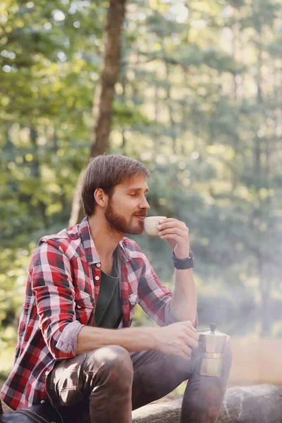 Kırmızı ekose gömlekli yakışıklı ormanda taze kahvenin tadını çıkarıyor.