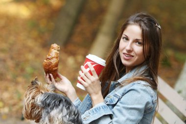 Güzel bir kadın köpeğiyle parkta dolaşırken yemek yer.