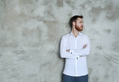 Beyaz gömlekli yakışıklı adam gri duvarda poz veriyor.