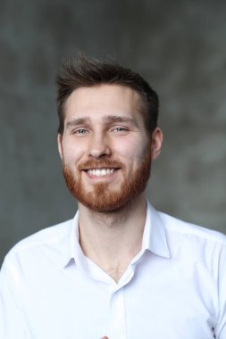 Beyaz gömlekli yakışıklı adam gri duvarda poz veriyor.