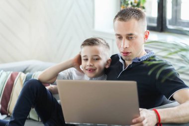 Baba ve oğul evde dizüstü bilgisayardan film izliyorlar.