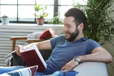 Evde sakallı yakışıklı bir adam kitap okuyor.