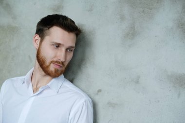 Beyaz gömlekli yakışıklı adam gri duvarda poz veriyor.