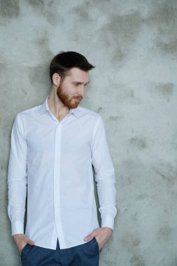 Beyaz gömlekli yakışıklı adam gri duvarda poz veriyor.