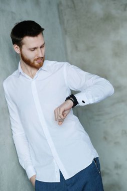 Beyaz gömlekli yakışıklı adam gri duvarda poz veriyor.