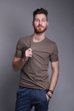 Gri arka planda poz veren rahat giyimli yakışıklı bir genç.