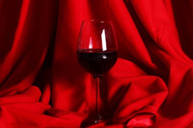 Kırmızı kumaşın üzerinde bir kadeh kırmızı şarap.