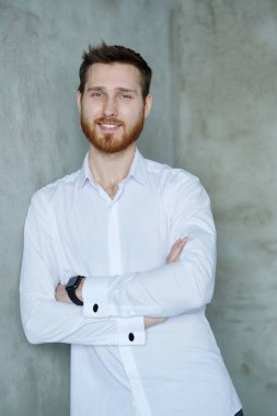 Beyaz gömlekli yakışıklı adam gri duvarda poz veriyor.
